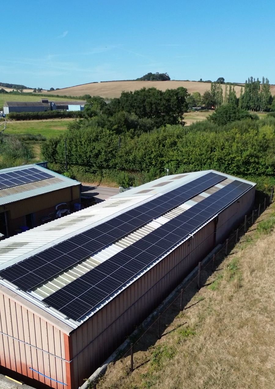 Long rows of solar panels on farm buildings with Devon hills behind