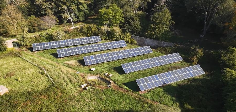 Five rows of ground-mounted solar panels in a walled garden